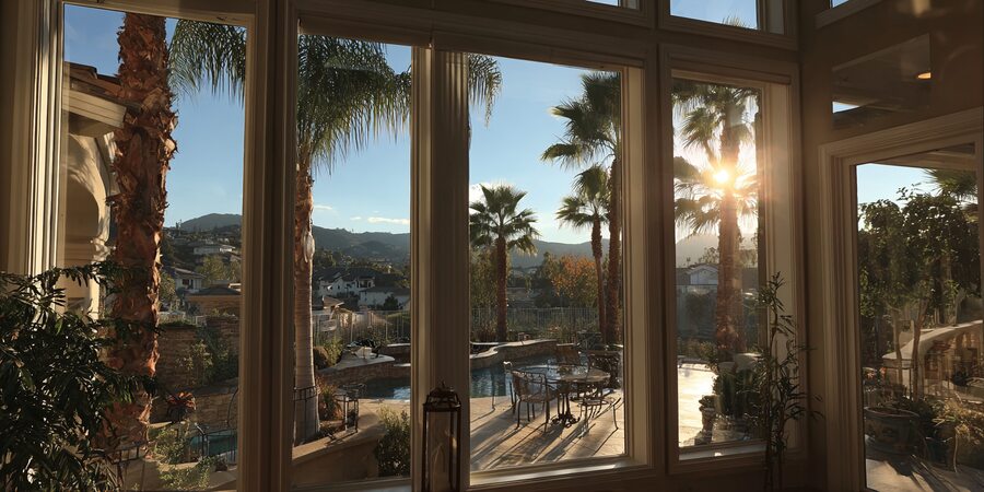 Sunlight through large Huntington Beach, CA windows overlooking palm trees, pool, and scenic hillside view.